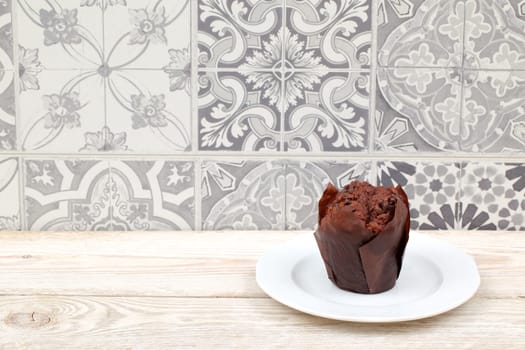 A delicious chocolate muffin sits elegantly on a white plate, beautifully displayed against a patterned backdrop