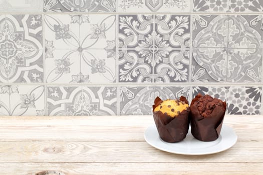 Two tempting muffins on a white plate against a vintage tile backdrop create an inviting scene to indulge