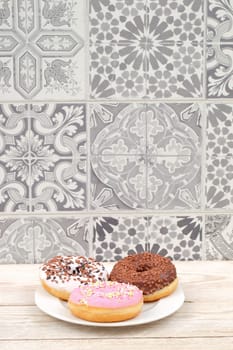 A colorful trio of mouthwatering donuts with lively icing, beautifully displayed on a decorative tile background
