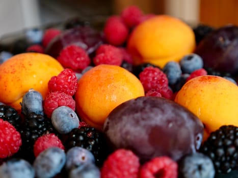 Colored background of seasonal summer fruits apricot, plum, raspberry, blueberry, blackberry in garden, close up