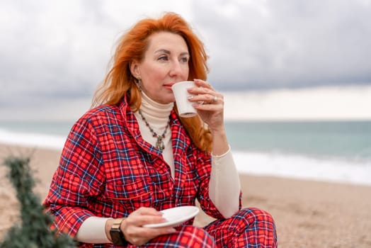 Sea Lady in plaid shirt with a mug in her hands enjoys beach with Christmas tree. Coastal area. Christmas, New Year holidays concep.