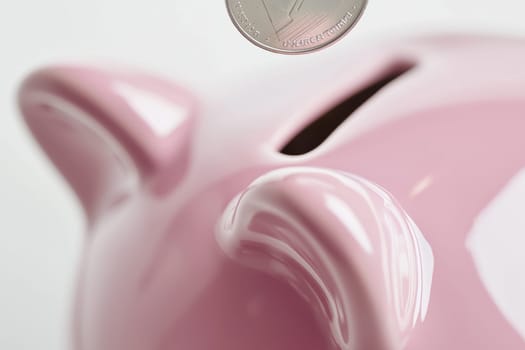 Close-up view of a soft pastel pink ceramic piggy bank as a shiny coin is inserted into the slot. set against a minimalist white background with a subtle reflection, emphasizing themes of savings and financial planning.