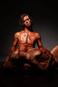 Nude man sitting on the floor and woman lying near both in blood shot in the dark room