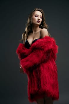 Gorgeous sexy girl wearing a red fur coat and luxurious bra portrait against dark wall