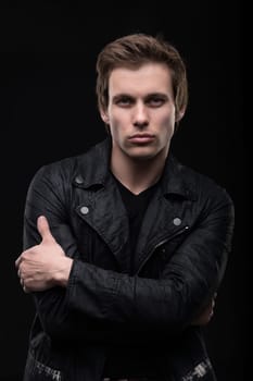 Handsome man in black leather jacket waist up shot against black wall