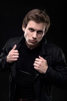 Resolute man in black leather jacket waist up shot against black wall