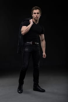 Charming sexy male in black jeanswear full-length shot in the dark room