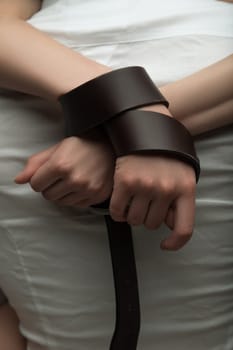 Girls hands tied up with a leather belt close up view