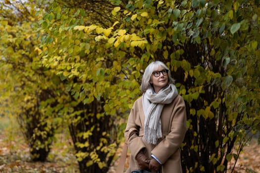 A woman stands thoughtfully among trees adorned with vibrant autumn leaves. She wears a warm coat and scarf while appreciating the beauty of the season.