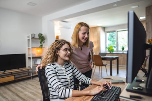 Two women are seated in front of a computer monitor, focusing on the screen as they engage in work or discussion. They appear to be deep in concentration, possibly collaborating on a project or analyzing data.