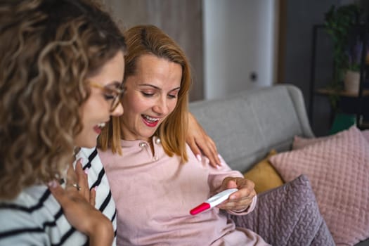 Two female friends are sitting on the couch in the living room, hugging and excited after getting their pregnancy test results.