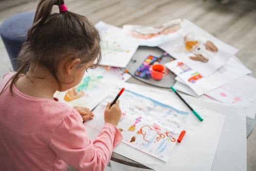 A young artist happily creates vibrant drawings on a table filled with artworks.