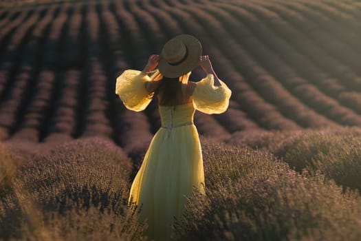 Here's a caption that meets your criteria: Woman in yellow dress and straw hat stands in a vast lavender field, back to camera, adjusting her hat. Golden sunlight bathes the scene.