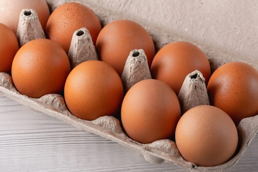 Fresh brown eggs in a cardboard carton arranged on a light wooden surface showcasing a farm-fresh collection ready for cooking.