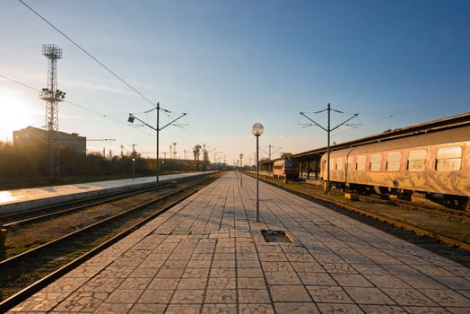 A quiet European railway station at sunset with a graffiti-covered train, empty platform, and nostalgic travel vibes.