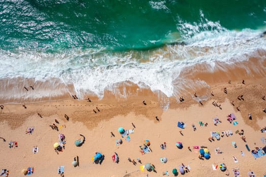 Overhead drone view of anonymous tourists and parasols on sandy seashore. Directly above shot of people enjoying summer vacations at beach during sunny day.