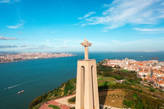 Aerial drone view of monument Sanctuary of Christ the King. Majestic scenery statue overlooking cityscape Almada and Tagus River. Bird's eye view Catholic monument and city.