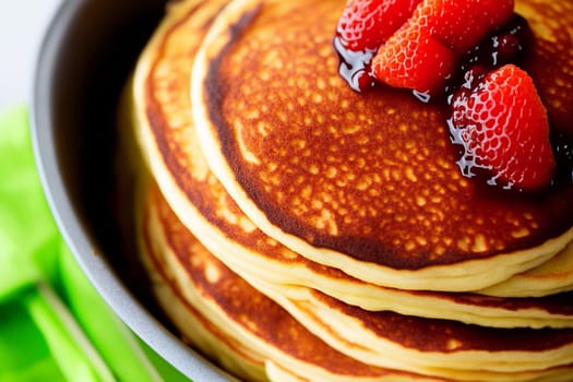 A stack of pancakes with strawberries on top. The pancakes are golden brown and look delicious. The strawberries add a pop of color and freshness to the dish