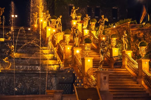 Fountain with cascades decorated with beautiful statues illuminated at night