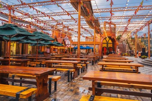 Decorated interior of the festive outdoor cafe restaurant with wooden tables and benches in the evening in Ba Na Hills Park. Da Nang, Vietnam - September 13, 2024