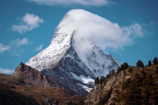 Beautiful photo of the famous Matterhorn with a hat of clouds forming around its pyramidal point. Taken from Zermatt ski and snowboard village, Switzerland.