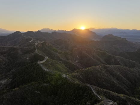 The sun rises over the rolling hills of the Great Wall of China as the manmade structure snakes along the landscape