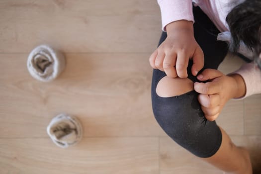 A child carefully adjusts a knee pad, while cozy and comfortable slippers lay on the floor