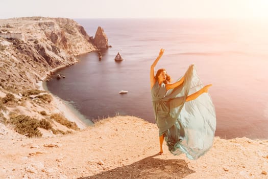 Woman green dress sea. Female dancer posing on a rocky outcrop high above the sea. Girl on the nature on blue sky background. Fashion photo