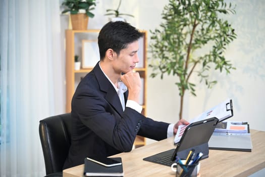 Satisfied millennial businessman checking documents in modern office.