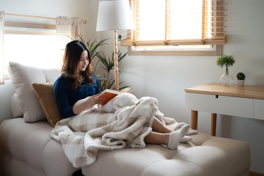 Calm adult woman reading book in living room with natural light streaming through the window.
