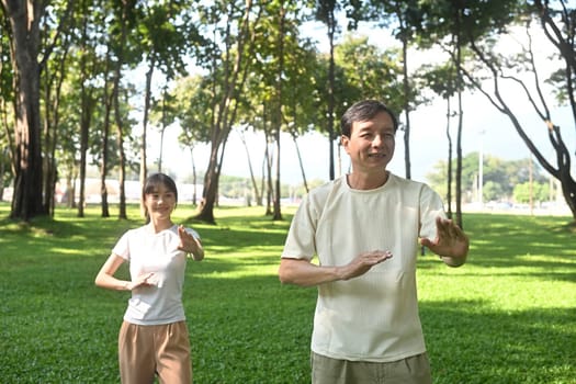 Calm father and daughter practicing Tai Chi in a serene park. Family activities, health and well being concept.