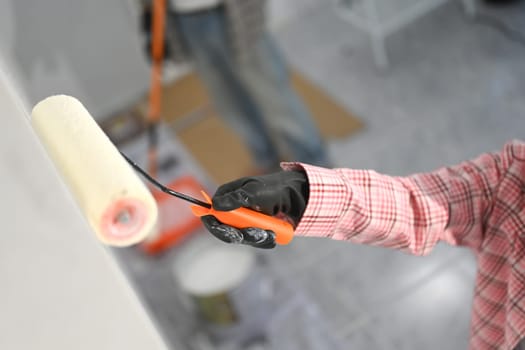 Close up of man painting a wall with a roller brush. DIY renovations and home improvement concept.