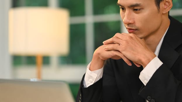 Serious and thoughtful businessman holding hands under chin looking at his laptop.
