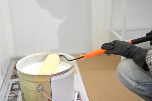 Close up shot of worker dipping a roller brush into can of white paint during a home improvement project.