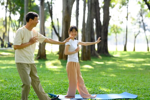 Active middle age man and his daughter practicing Tai Chi in a serene park. Health and well being concept.