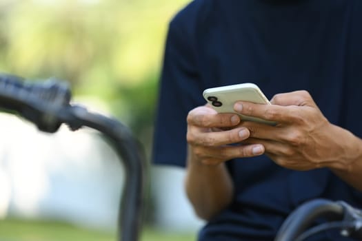Close up young man using smartphone while sitting at the park with bicycle.