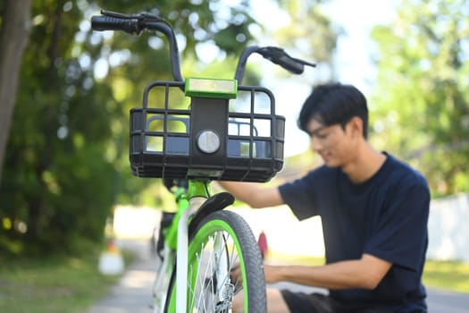 Asian male fixing a bicycle chain in the park on the summer day.