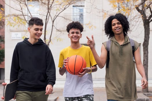 three diverse teenager friends with basketball and skateboard talking while having fun walking on the street, concept of youth and urban lifestyle