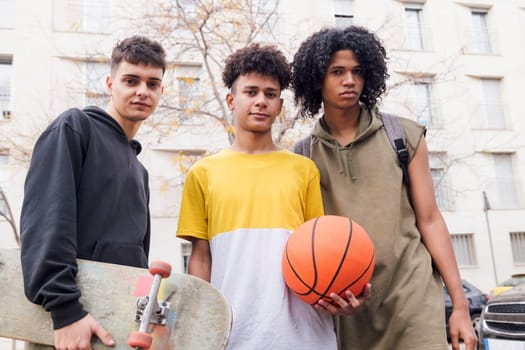 three diverse teenager friends with basketball and skateboard standing together looking at camera, concept of youth and urban lifestyle