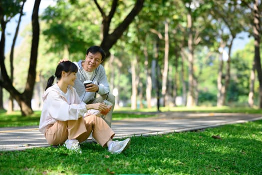 Delightful middle age man and his daughter enjoy refreshing drinks while taking a break from exercising in a park..