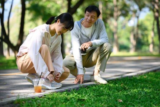 Father and daughter tying shoelaces before jogging in a beautiful park. Health and wellbeing concept.