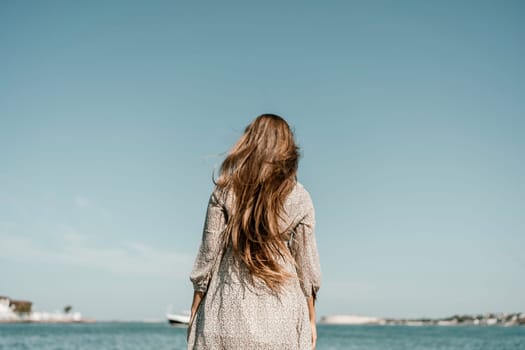 woman with long hair stands in front of a blue sky. She is wearing a white and black striped shirt