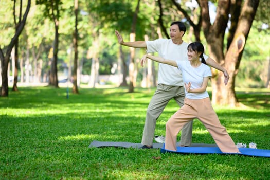 Father and daughter practicing Tai Chi together in the park with sunlight streaming through foliage. Health and well being concept.