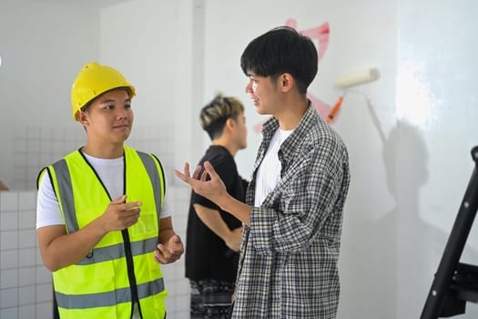Shot of supervisor in hardhat discussing plans with painter standing inside house.