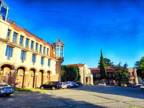 Sighnaghi, Georgia - June 06, 2024: Historic architecture and tall trees frame a peaceful square under a bright blue sky at midday, inviting leisurely exploration.