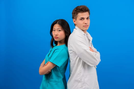 Confident doctor and nurse standing back-to-back with arms crossed, serious on a vibrant blue background. The image highlights teamwork, professionalism, and positivity in healthcare.