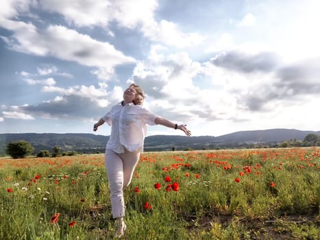 A happy girl in a poppy field. The journey of a middle-aged woman in summer. A tourist on trip