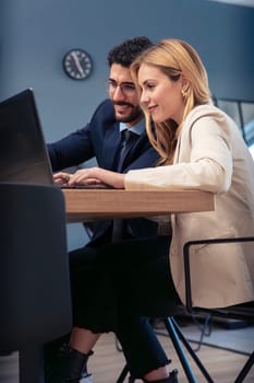 A man and a woman collaborate in a modern office, sharing a laptop screen while working on a project. They smile at each other, showing a productive and friendly business partnership.Vertical