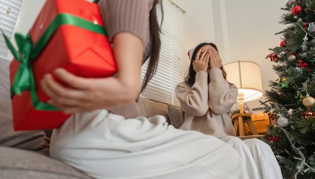 Happy young woman couple exchanging gifts and celebrating Christmas in a cozy home environment, filled with festive decorations.