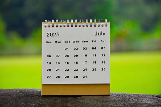 July 2025 white calendar with green blurred background.